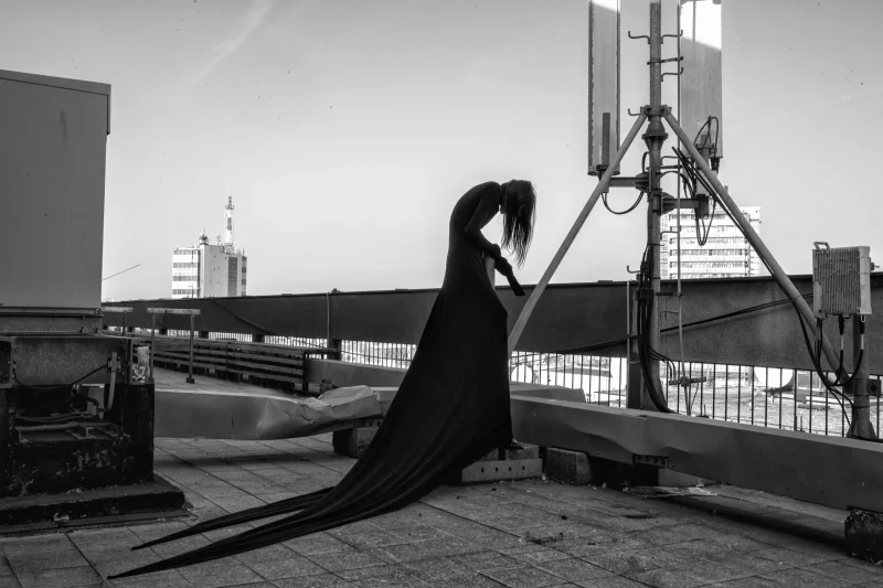 TESKOBA: model in a black trained gown bending forward beneath a rooftop antenna mast