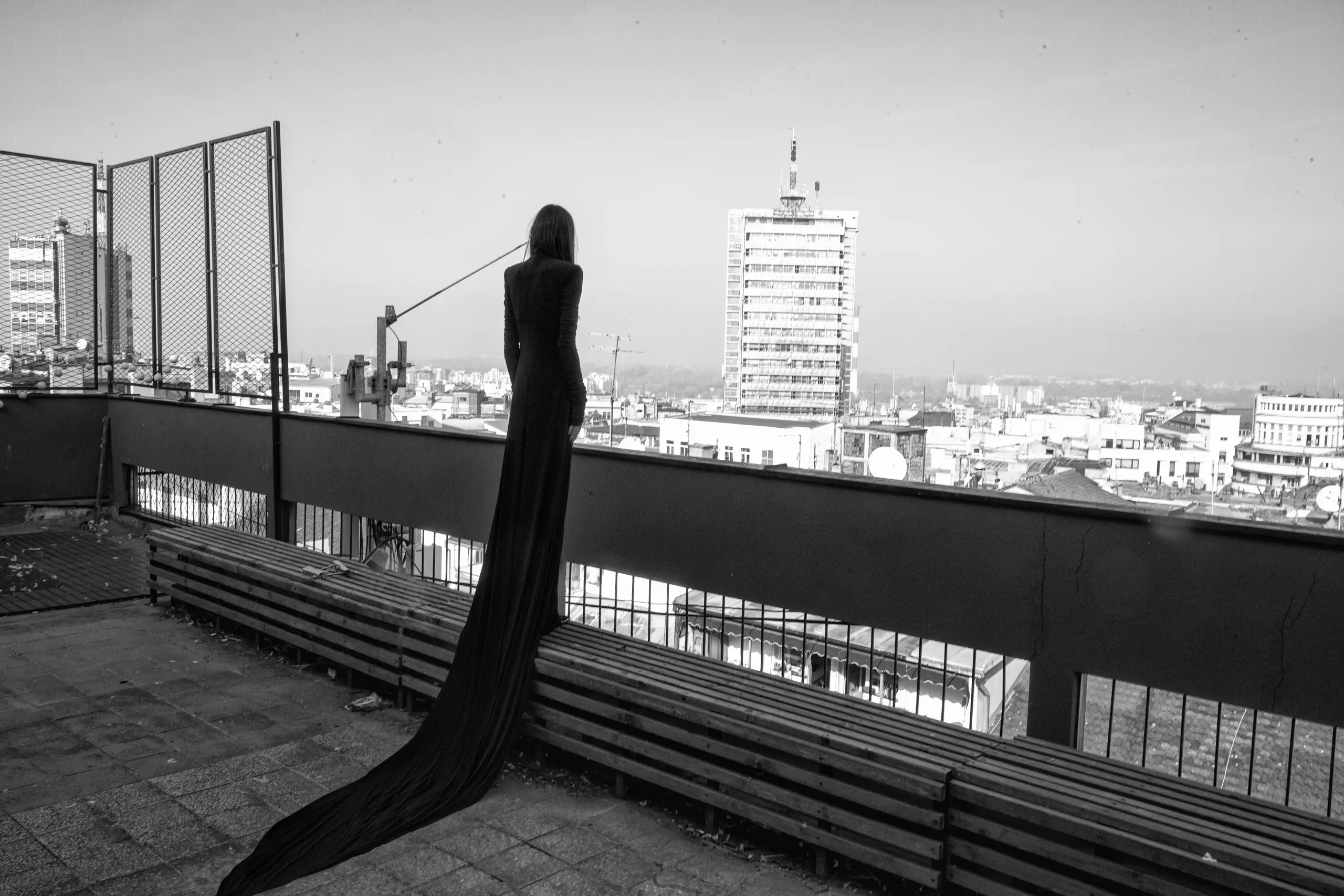 TESKOBA: model seen from behind in a black gown with a long train, overlooking Belgrade rooftops