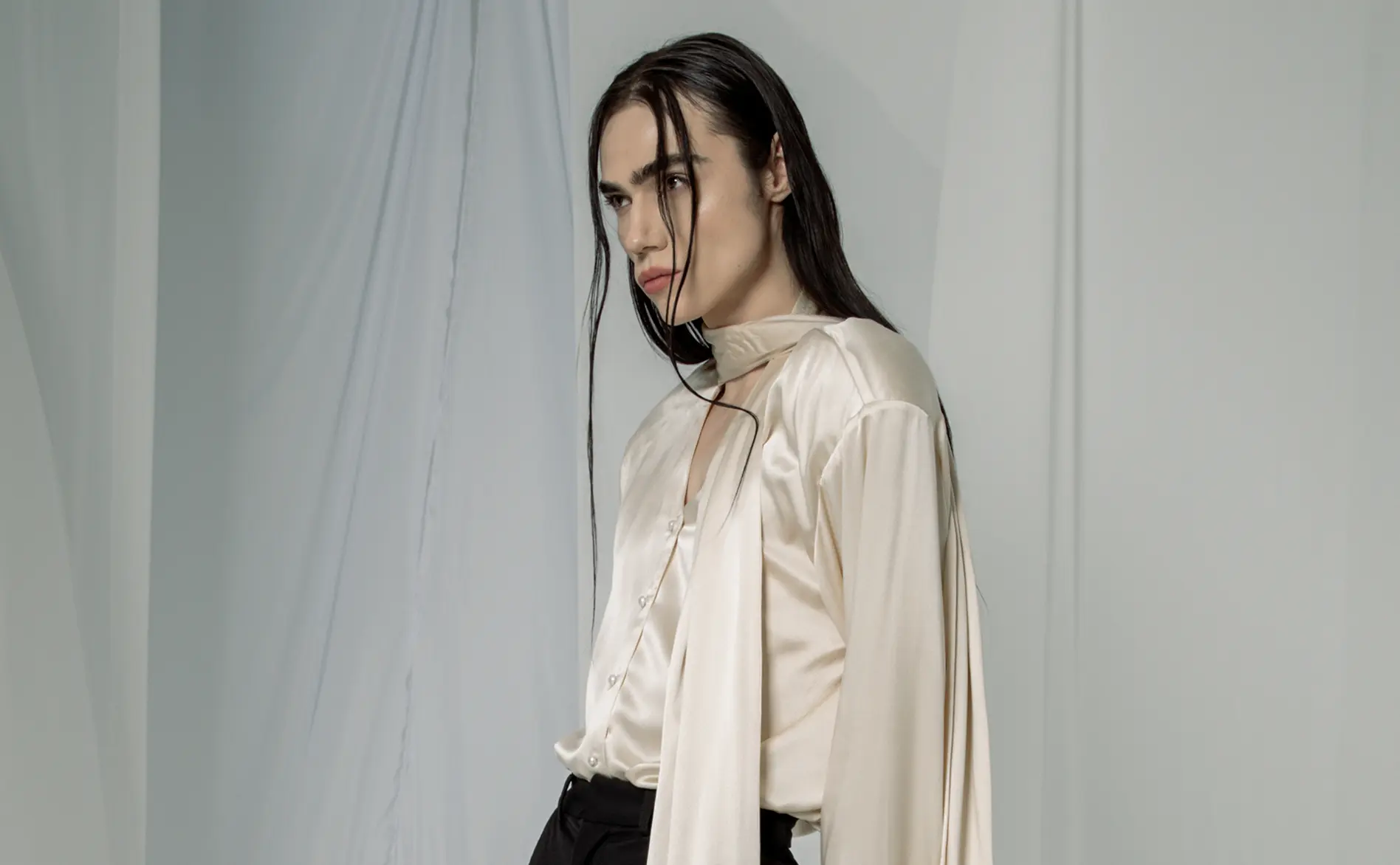 Model in profile wearing an ivory satin blouse with a keyhole neckline and long neck tie