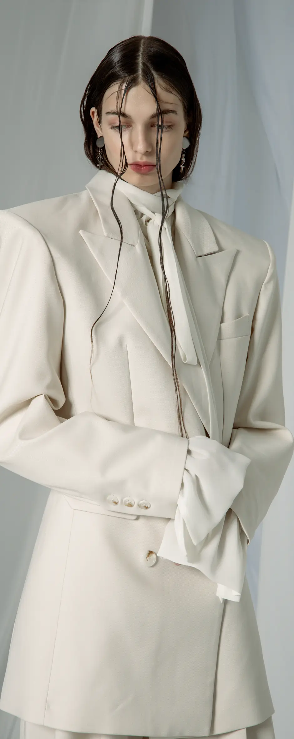 Model in an ivory oversized blazer with strong shoulders over a tie-neck blouse with ruffled cuffs