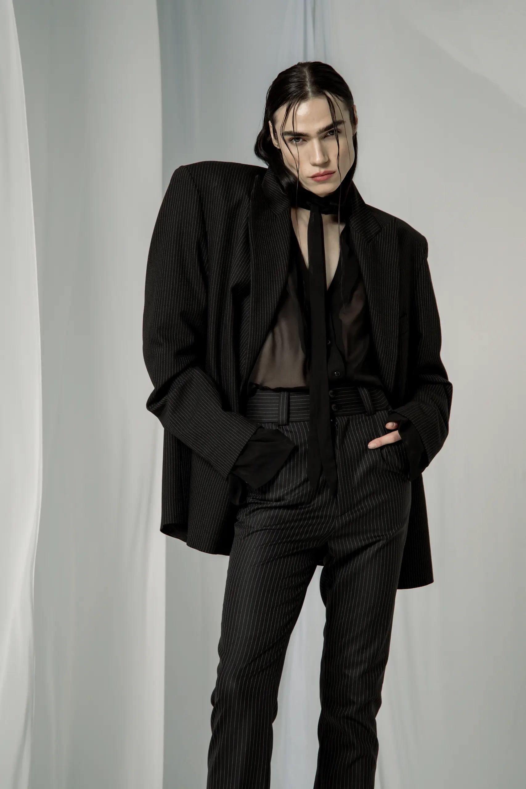 Oversize sako na tanke pruge preko providne bluze, pantalone visokog struka, ruka u džepu