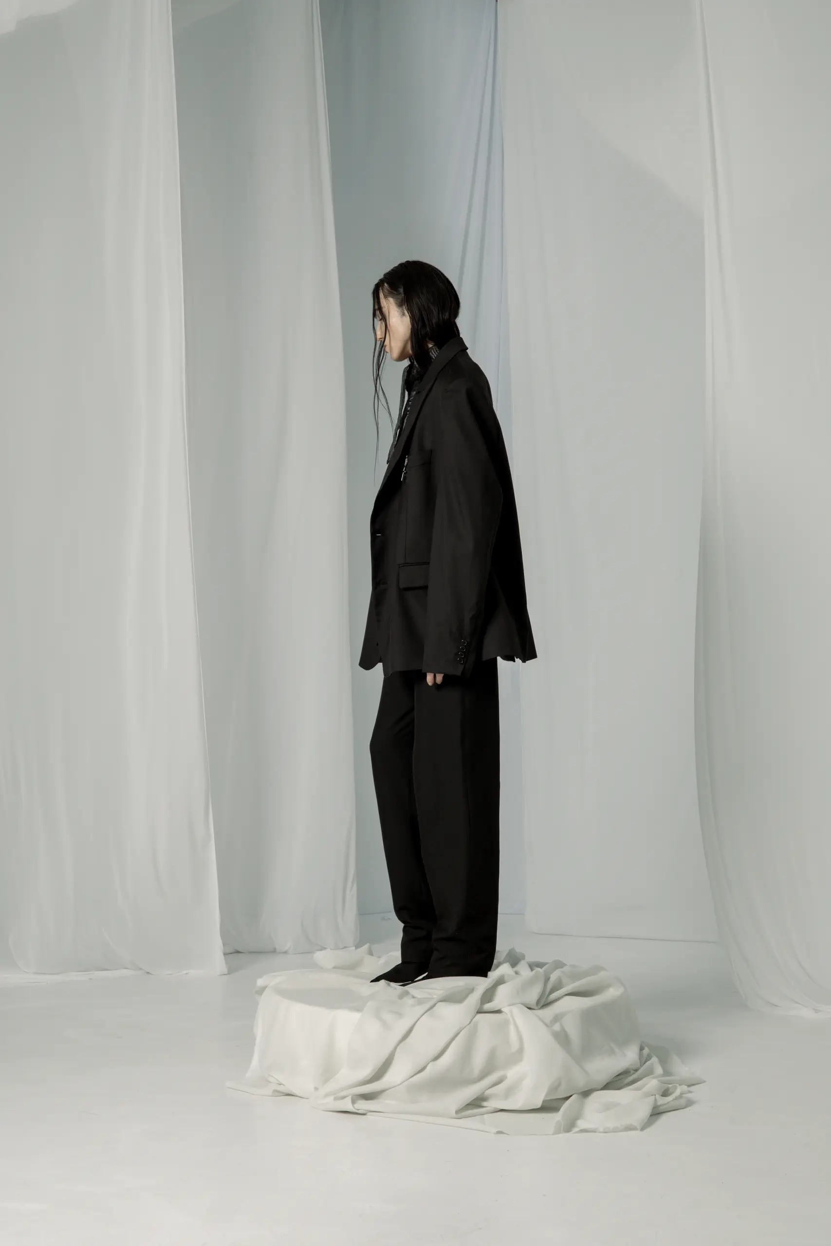 Oversize crni sako i ravne pantalone, model iz profila na drapiranom postamentu