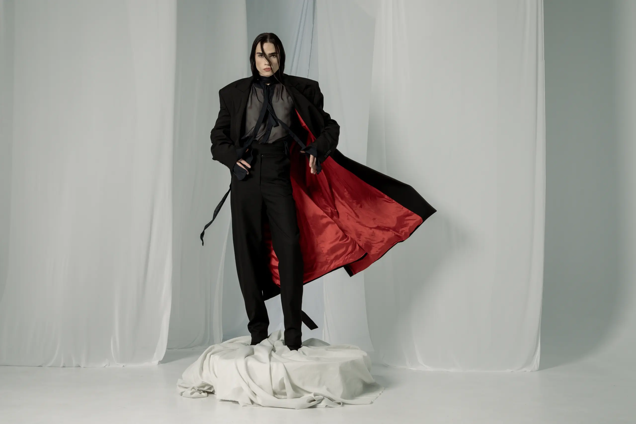 Oversize crni kaput sa crvenom satenskom postavom koja se razvija, prozirna bluza i crne pantalone