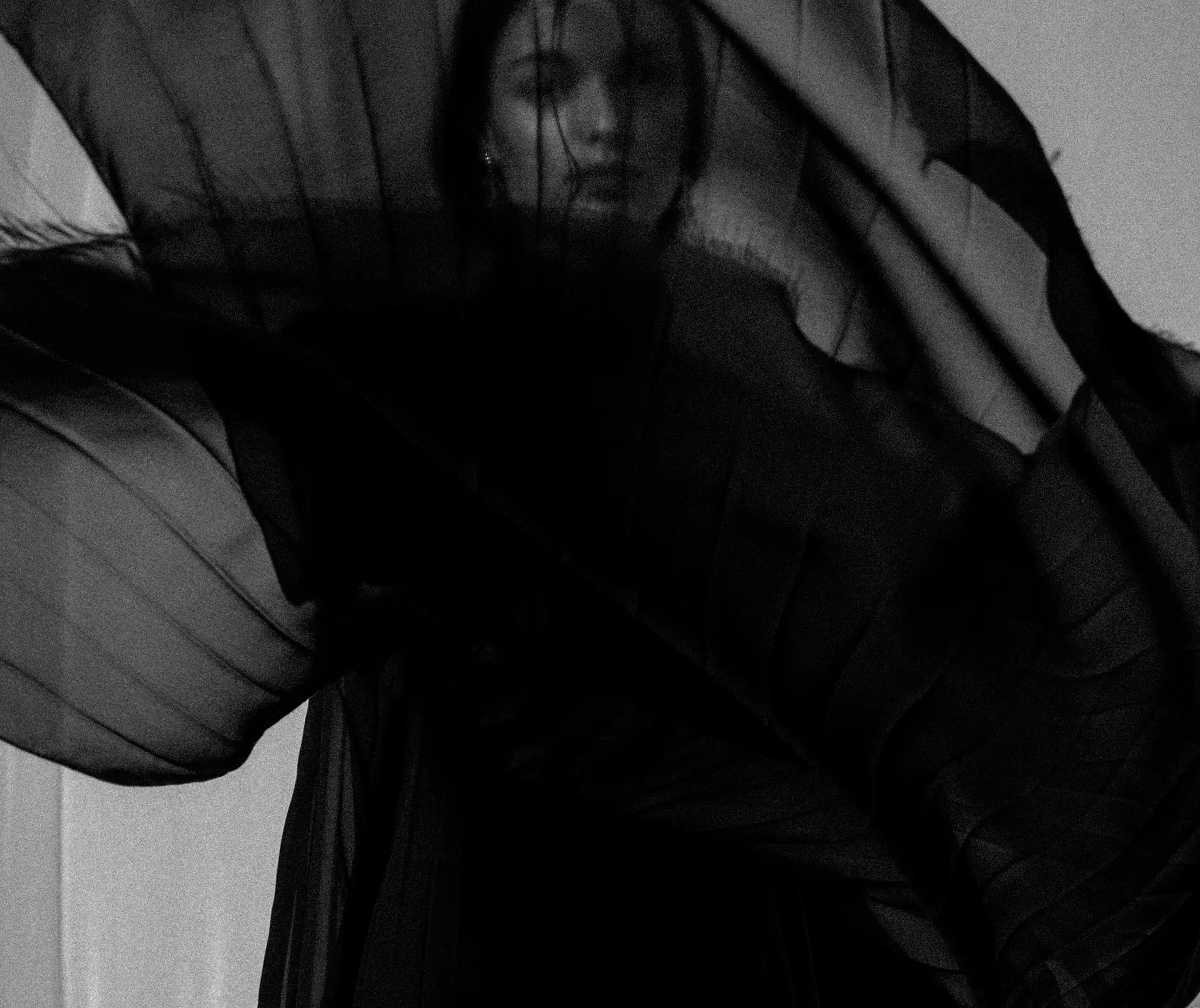 Model partly veiled by sheer black pleated chiffon in motion, in black and white